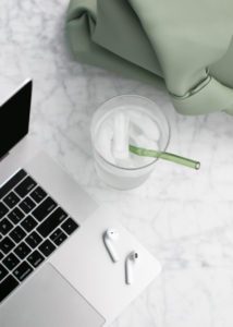 Picture of water with drinking straw beside a laptop and earbuds.