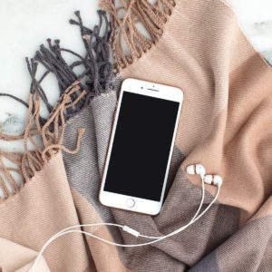 Picture of a brown scarf with an iphone and headphone laying on it showing it needs to be away for scarf storage. 