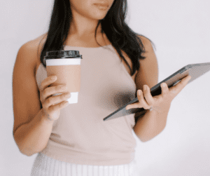Image of Woman holding an Ipad in one hand, and a coffee in the other.
