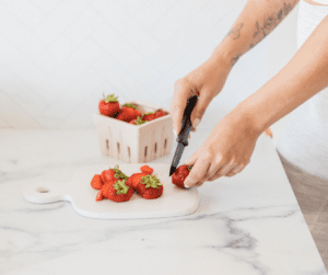Image of woman cutting up strawberries on a marble counter.