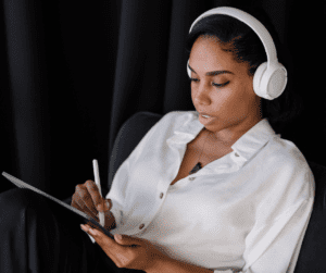 Image of a woman in headphones sitting in a black chair who is writing on a tablet with a white stylus. Showing grow your email list with pinterest marketing.