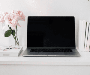 Image of a computer sitting on a desk with roses in a glass vase beside showing a workspace for Pinterest virtual assistant or Pinterest Manager. 