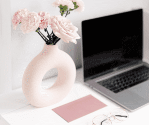 Image of a desk with rose and blush items such as a note card, glasses and vase with flowers. This shows a desk set up for a pinterest virtual assistant. 