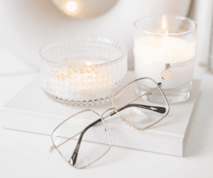 Image of glasses sitting on a closed white book with a 2 lit candles behind showing virtual assistant work station. 