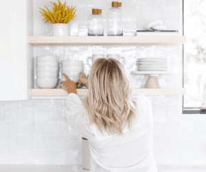 Image of a woman putting away clean dishes, reaching to open shelves to put away bowls. 