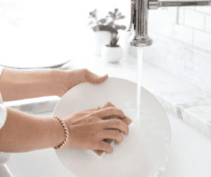 Image of a woman cleaning a dish over her sink, showing the importance of summer cleaning your sink. 