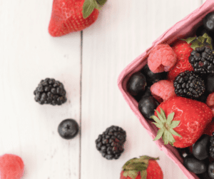 Image of blueberries, strawberries and raspberries in a berry carton and on a white counter. 
