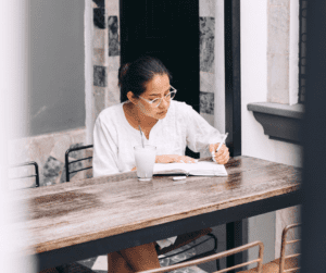Woman witting at wooden table writing down a list of unique blog ideas! 