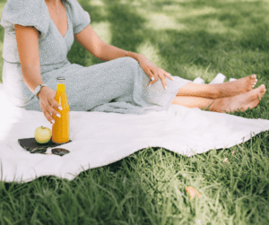 Woman sitting on a blanket on some grass enjoying the summer with a fresh orange juice beverage. 