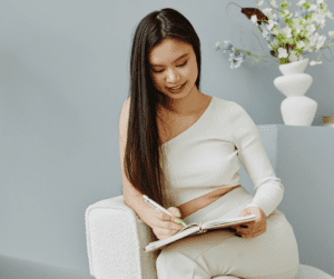Image of a woman sitting on a chair using an notepad and pen to take time to learn how to plan your week to be productive! 