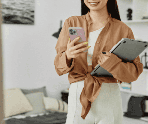 Image of a woman holding an iphone in one arm and carrying a closed laptop under her other arm. 
