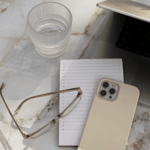 Image of desk items such as glasses, cup of water, iphone, and notepad. 