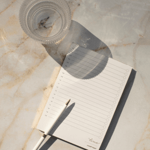 Image of a blank notepad and cup of water on a marbled counter. 