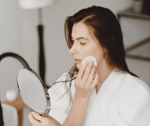 A woman looking in a handheld mirror removing make up and creams as part of the process for getting a facial. 