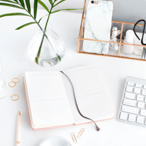 Image of items on a desk such as journal, keyboard and vase.
