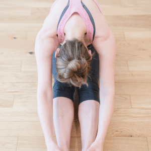 Image of woman sitting on floor doing stretches for menstrual cramps. 