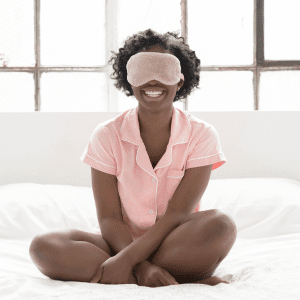 Image of woman sitting up in bed with eye mask to help with good sleep quality. 
