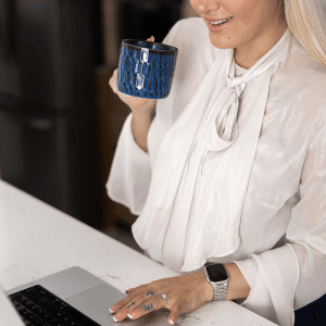 Image of woman sipping coffee from a dark blue mug as she clicks on a laptop about do you need a blog for pinterest.