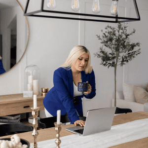Image of woman leaning over a wooden table working on a laptop.