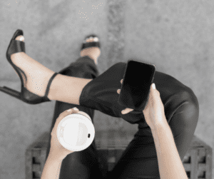 Image of woman sitting with a coffee in one hand and her phone in the other on a chair.
